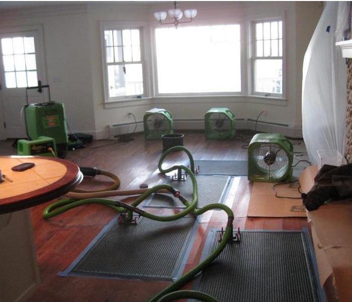 three taped down 2x4 feet drying mats, with assorted green fans in this living room drying the redwood looking floor